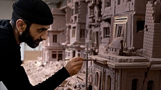 Syrian sculptor Khaled Dawwa works on a clay artpiece, representing a street in Syria destroyed by Syrian regime forces, in his workshop in Vanves, near Paris, January 9, 2022