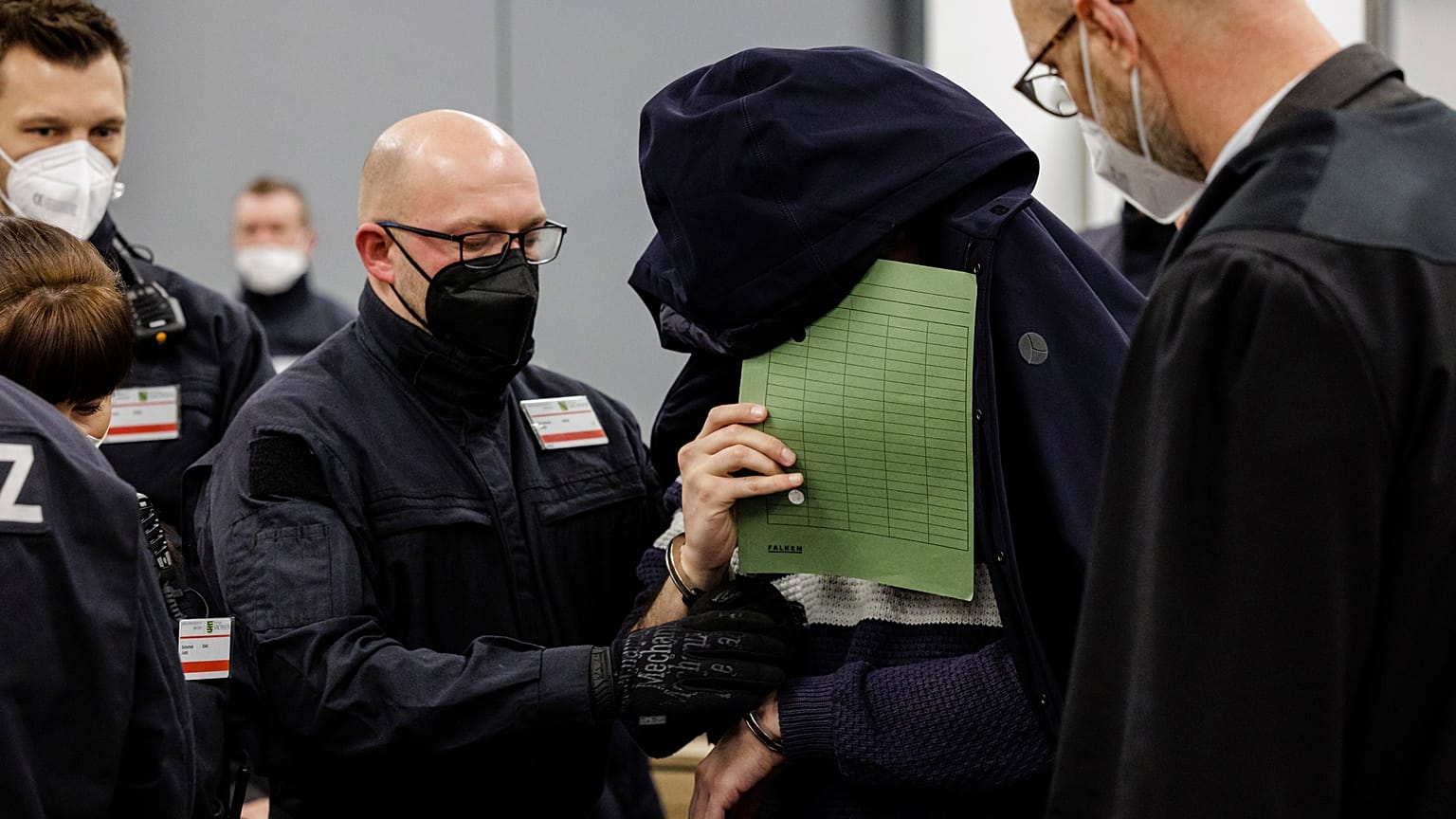 Einer der Angeklagten betritt das Landgericht Dresden in Handschellen und verdeckt sein Gesicht.