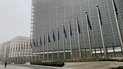 A woman walks in the fog past EU flags in front of EU headquarters in Brussels, Jan. 25, 2022.