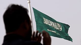 رجل يصلي أمام علم سعودي عملاق في جدة بالمملكة العربية السعودية. 