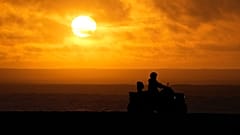 A person drives a quad bike along the beach as the sun sets in Nazare, Portugal, Saturday, Dec. 11, 2021. 