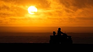 A person drives a quad bike along the beach as the sun sets in Nazare, Portugal, Saturday, Dec. 11, 2021.