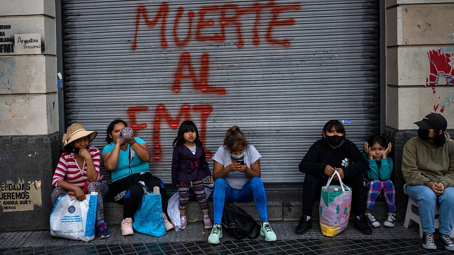 Des manifestants assis devant un graffiti où l'on peut lire en espagnol "Mort au FMI" après une manifestation à Buenos Aires (Argentine), mardi 8 février 2022. 