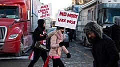 People walk in front of trucks parked on Wellington Street as they join a rally against COVID-19 restrictions on Parliament Hill