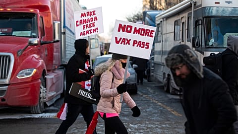 People walk in front of trucks parked on Wellington Street as they join a rally against COVID-19 restrictions on Parliament Hill