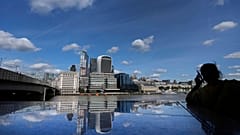 A woman is silhouetted as she takes a phone call, as the skyline of London is reflected in the polished stones of London Bridge during sunny weather in London, Tuesday, Sept. 