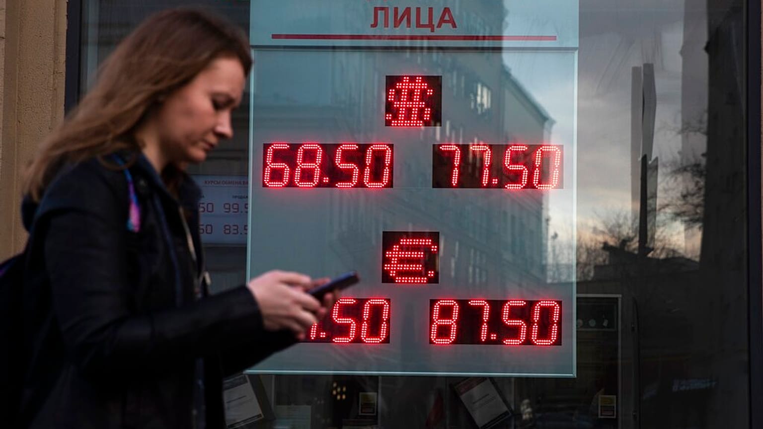 A woman walks past an currency exchange office screen displaying the exchange rates of U.S. Dollar and Euro to Russian Rubles, in Moscow.