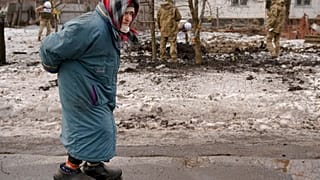 An elderly lady walks by as members of the Joint Centre for Control and Coordination on ceasefire of the demarcation line