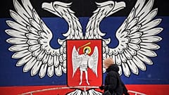 Une habitante de Donetsk passant devant un mur de la ville recouvert de l'emblème de la République populaire de Donetsk, le 19 janvier 2022