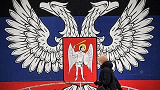 Une habitante de Donetsk passant devant un mur de la ville recouvert de l'emblème de la République populaire de Donetsk, le 19 janvier 2022