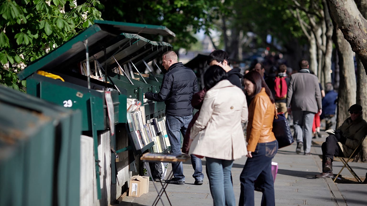 People look at books and posters as they walk past booksellers "bouquinistes", near the river Seine