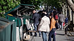 People look at books and posters as they walk past booksellers "bouquinistes", near the river Seine