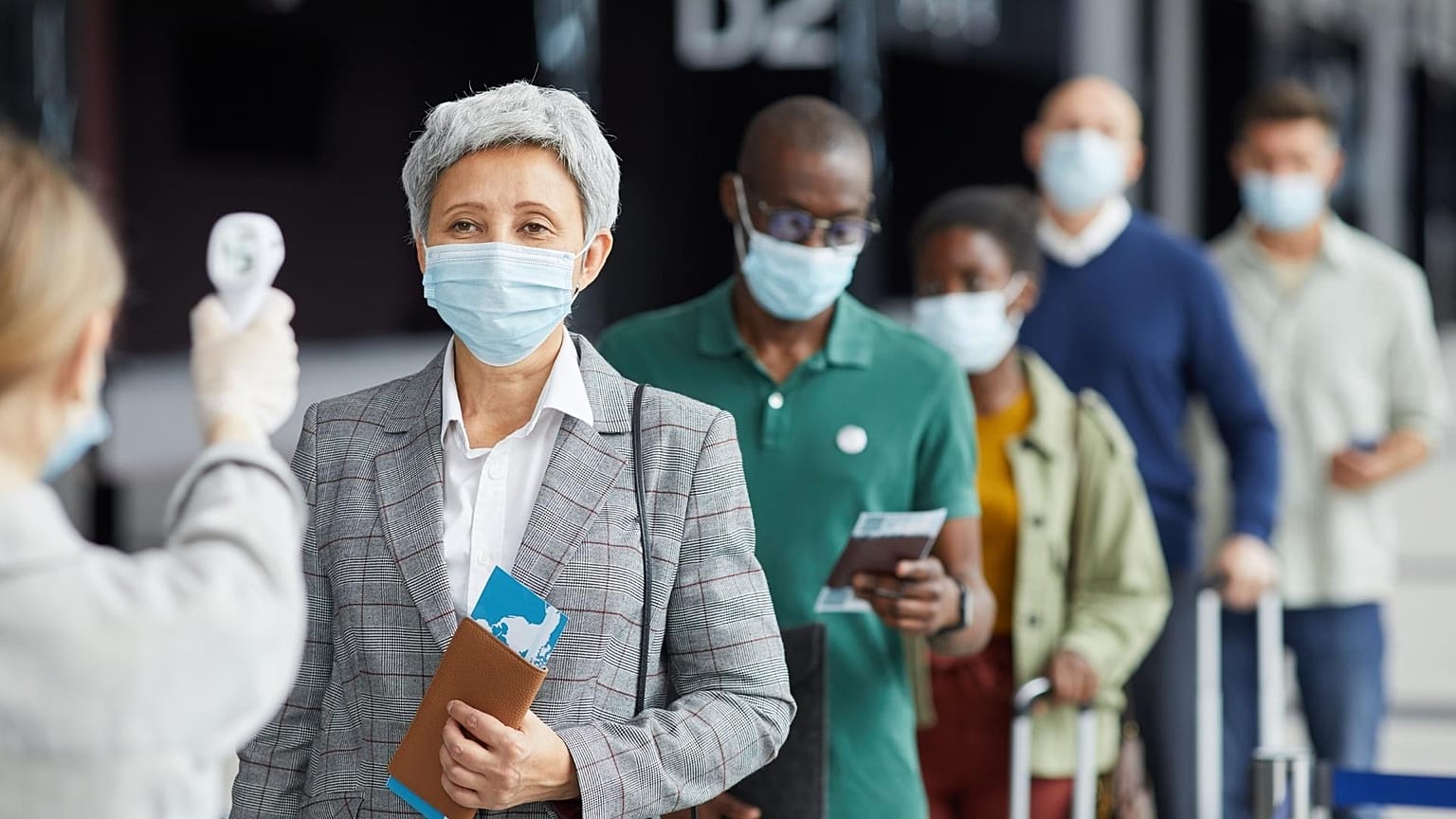A line of people wait to have their temperature checked at an airport