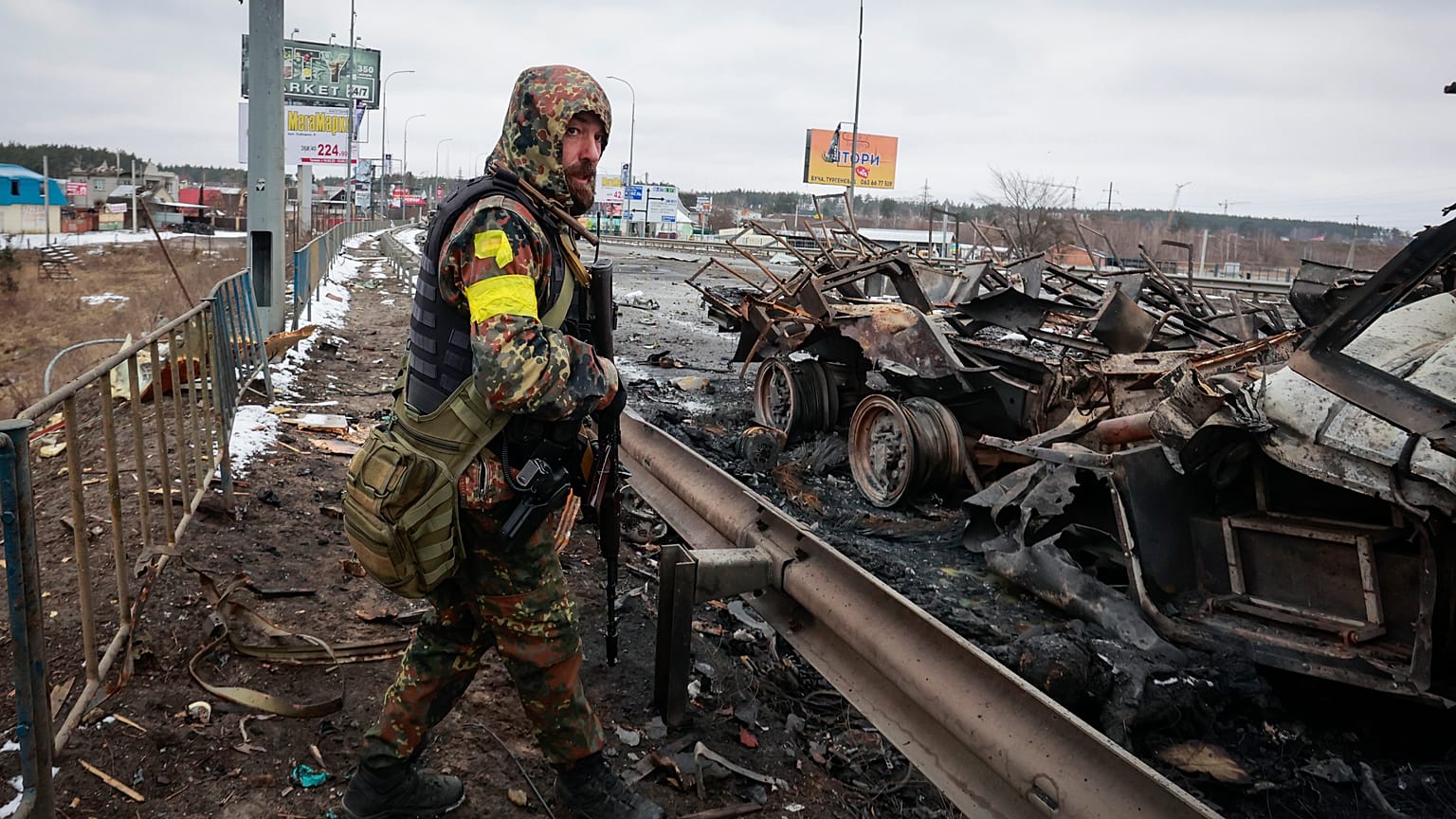 An armed man stands by the remains of a Russian military vehicle in Bucha, close to the capital Kyiv, Ukraine, Tuesday, March 1, 2022.