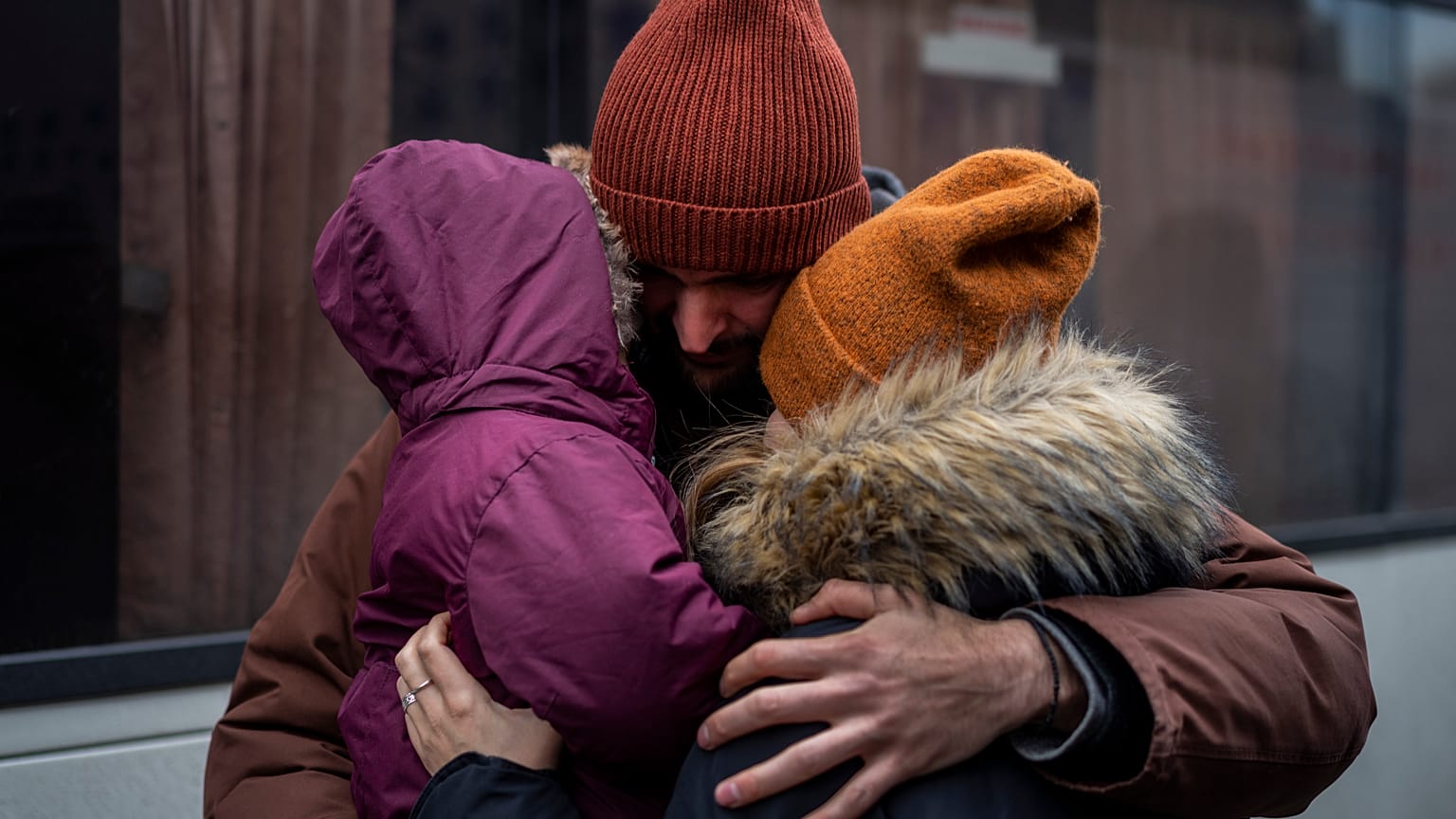 Kyiv resident, holding his daughter and hugging his wife, next to bus destined for Poland at Lviv central station.