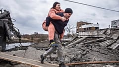 Un hombre lleva a una mujer mientras cruzan un camino improvisado mientras huyen de la ciudad de IrpÍn, Ucrania, el domingo 6 de marzo de 2022
