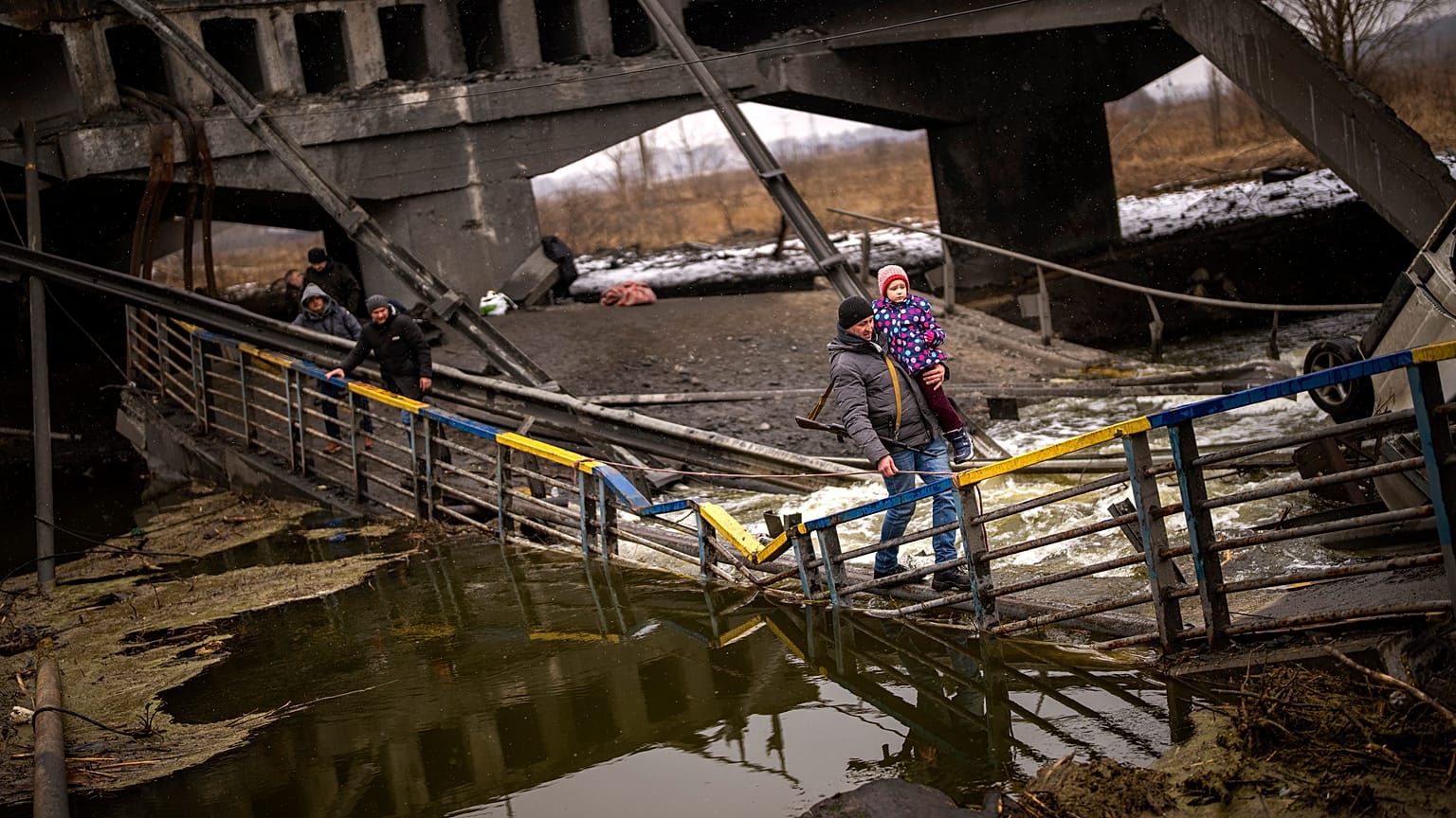 Local militiaman Valery, 37, carries a child as he helps a fleeing family across a bridge destroyed by artillery, on the outskirts of Kyiv, Ukraine, Wednesday, March 2. 2022