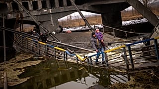 Local militiaman Valery, 37, carries a child as he helps a fleeing family across a bridge destroyed by artillery, on the outskirts of Kyiv, Ukraine, Wednesday, March 2. 2022