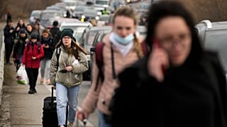 FILE - Ukrainian refugees walk along vehicles lining-up to cross the border from Ukraine into Moldova.