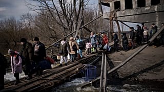 Ukrainians cross an improvised path under a destroyed bridge while fleeing Irpin, on the outskirts of Kyiv, Ukraine, Wednesday, March 9, 2022.