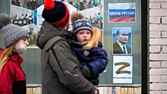 Egy család sétál el Szentpéterváron a gyermekkönyvtár előtt, ahol Putyin elnök portréja és az ukrán hoború szimbólumává vált Z betűt tettek a kirakatba