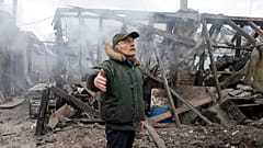 A man opens his arms as he stands near a house destroyed in the Russian artillery shelling, in the village of Horenka close to Kyiv