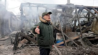 A man opens his arms as he stands near a house destroyed in the Russian artillery shelling, in the village of Horenka close to Kyiv