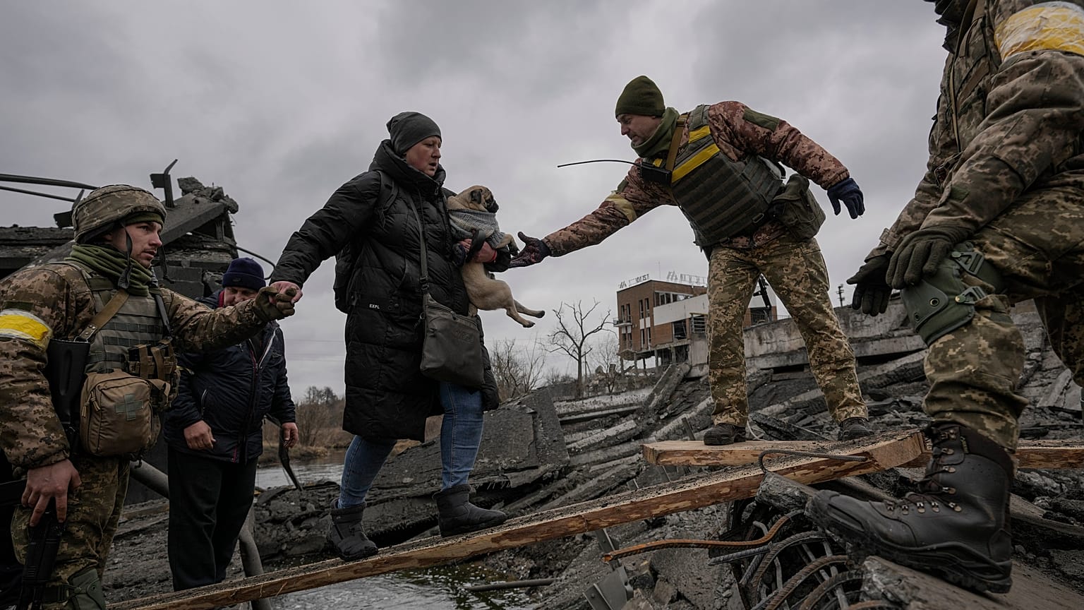 Ukrainian servicemen help a woman carrying a small dog across the Irpin River.