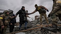 Ukrainian servicemen help a woman carrying a small dog across the Irpin River.