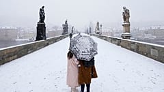 A couple crosses the medieval Charles Bridge as snow falls in Prague, Czech Republic, Friday, March 4, 2022.