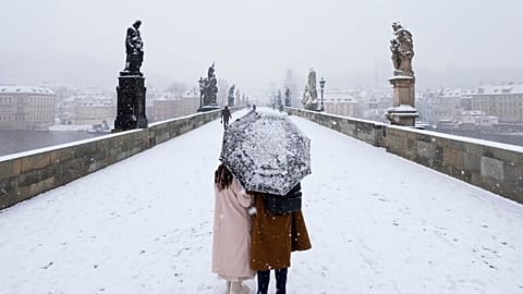 A couple crosses the medieval Charles Bridge as snow falls in Prague, Czech Republic, Friday, March 4, 2022.
