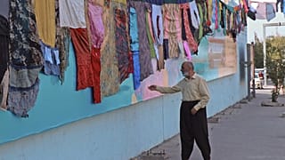  رجل عراقي أمام عمل فني للفنانة البصرية تارا عبد الله في مدينة السليمانية، يمثل ملابس مخيطة لنساء نجين من العنف الأسري لتسليط الضوء على المشكلة الاجتماعية المتفشية في العراق.