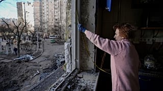 A woman measures a window before covering it with plastic sheets in a building damaged by a bombing the previous day in Kyiv, Ukraine, Monday, March 21, 2022.