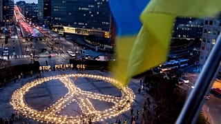 People stand around a giant peace sign with the message 'Stop Putin's Oil', put up by demonstrators ahead of an EU and NATO summit in Brussels, Tuesday, March 22, 2022.