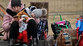 A woman with her child checks her mobile phone as she waits for relocation outside the main shelter and relocation center in Przemysl, southeastern Poland.