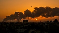 A passenger airplane flies over a smouldering fire at an Aramco oil depot after a Yemen Houthi rebel attack as the sun rises in Jiddah, 26 January 2022