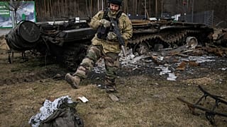 A Ukrainian serviceman kicks a burnt sleeping bag near the wreck of a Russian tank in Stoyanka, Ukraine, Sunday, March 27, 2022