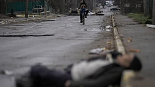 Un homme et un enfant sur une bicyclette avancent vers un cadavre à Boutcha, le 2 avril 2022