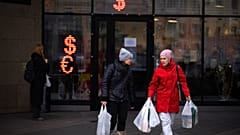Two women walk past a currency exchange office screen displaying the exchange rates of U.S. Dollar and Euro to Russian Rubles in Moscow