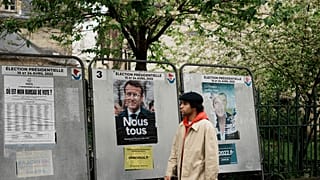 Un hombre pasa junto a los carteles rotos de la campaña presidencial de Emmanuel Macron y Marine Le Pen