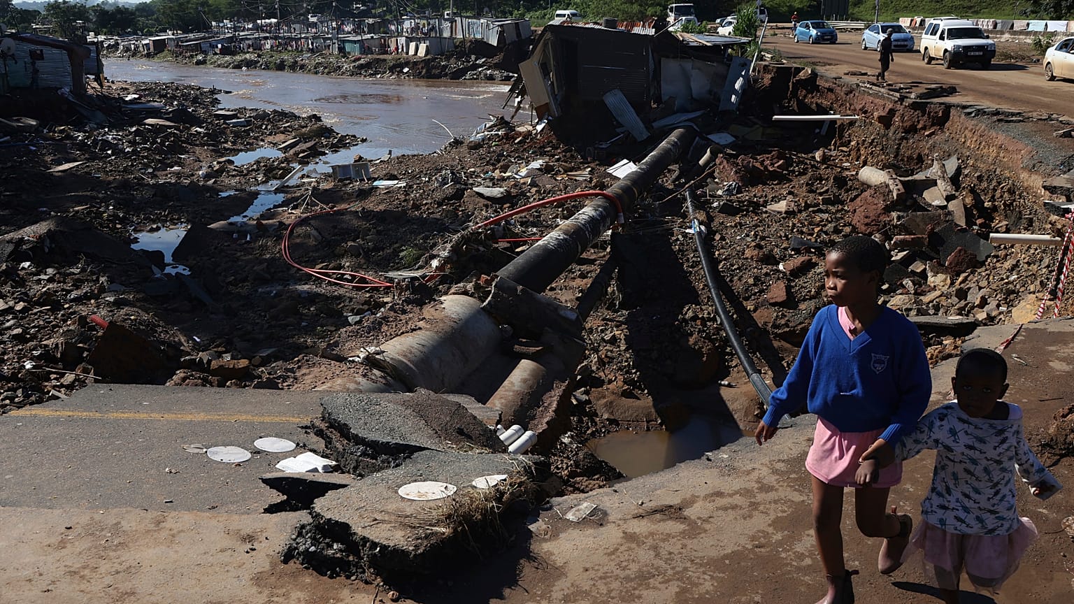 Unos niños caminan por una carretera dañada en un asentamiento informal en Durban, Sudáfrica, el jueves 14 de abril de 2022. 