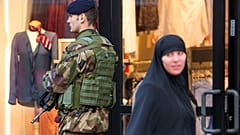 سيدة محجبة تسير أمام جندي يقوم بدورية في شارع روبيه بشمال فرنسا، في 13 يناير 2015.