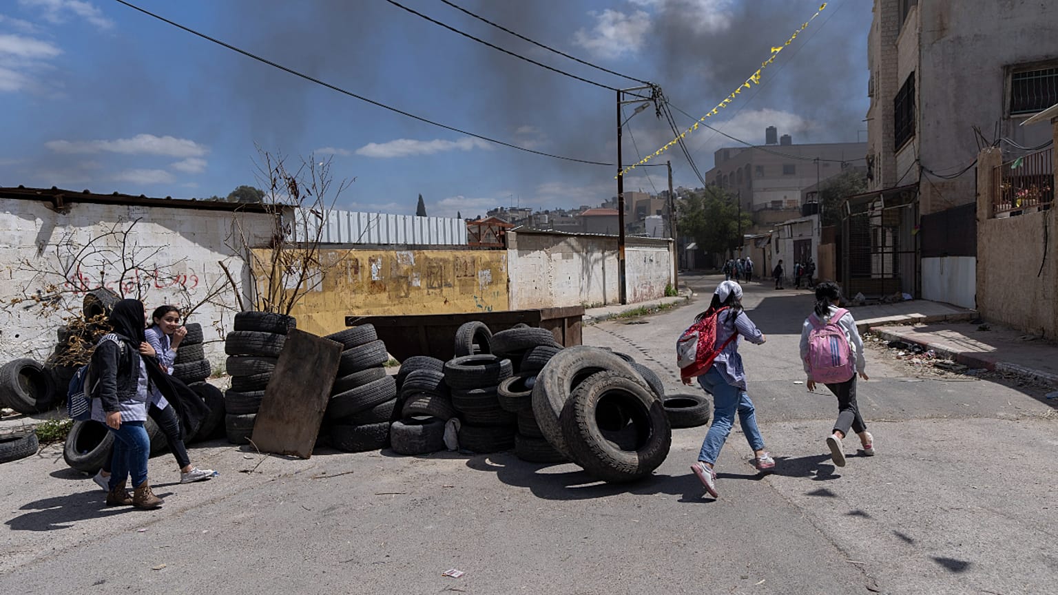 تلامذة فلسطينيون يسيرون بالقرب من أكوام إطارات تم جمعها لإضرام النار فيها أثناء التوغلات المحتملة للجيش الإسرائيلي في مخيم جنين للاجئين بالضفة الغربية، 12 أبريل 2022
