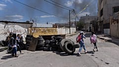 تلامذة فلسطينيون يسيرون بالقرب من أكوام إطارات تم جمعها لإضرام النار فيها أثناء التوغلات المحتملة للجيش الإسرائيلي في مخيم جنين للاجئين بالضفة الغربية، 12 أبريل 2022
