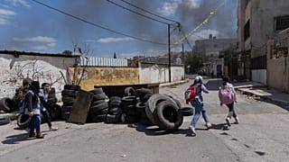 تلامذة فلسطينيون يسيرون بالقرب من أكوام إطارات تم جمعها لإضرام النار فيها أثناء التوغلات المحتملة للجيش الإسرائيلي في مخيم جنين للاجئين بالضفة الغربية، 12 أبريل 2022