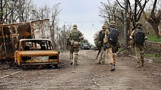 Servicemen of Donetsk People's Republic militia walk past damaged vehicles in an area controlled by Russian-backed separatist forces in Mariupol, April 19, 2022.