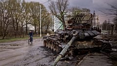Egy férfi biciklizik el egy tönkretett tank mellett Csernyihiv városában