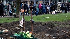 Menschen stehen Schlange auf einem behelfsmäßigen Straßenmarkt neben frischen Gräbern in Mariupol.