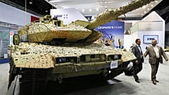 رجال يمشون بجوار دبابة ألمانية من طراز Krauss-Maffei Wegmann Leopard تحمل لافتة "تم البيع" في معرض الدفاع الدولي في أبو ظبي
