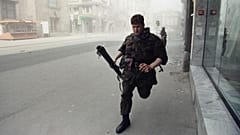 Bosnian army member sprints for cover after a tank round, fired by Yugoslav People's Army, struck an apartment house across the street in Sarajevo on 2 May 1992